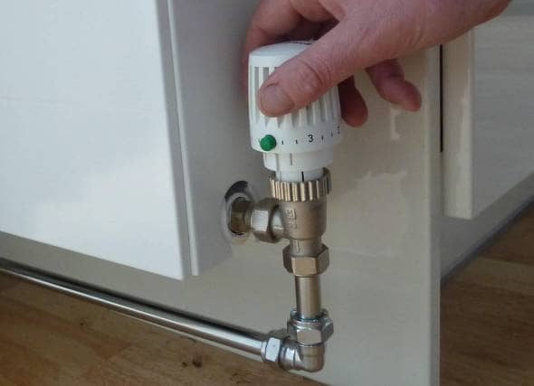 a hand turning the valve on a radiator after successfully balancing a heating system