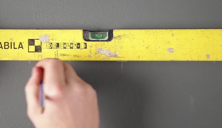 Man marking a line on a grey wall with a pencil and a spirit level