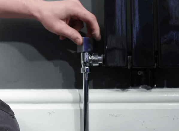 A hand turning a chrome radiator valve on a designer radiator