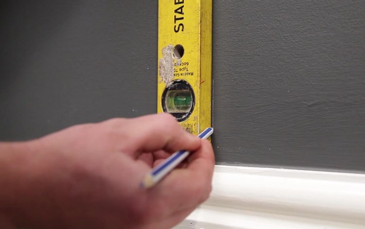 Man using a spirit level and a pencil to mark a line on the wall