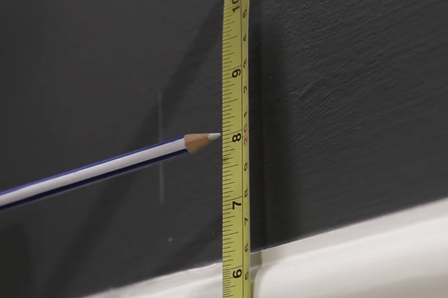 A pencil pointing to a tape measure on a wall above a skirting board
