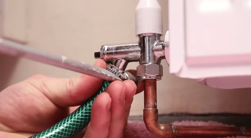 Man attaching a hosepipe to an angled drain off valve on a radiator