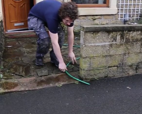 A plumber placing a hosepipe outside the front of a house and garden