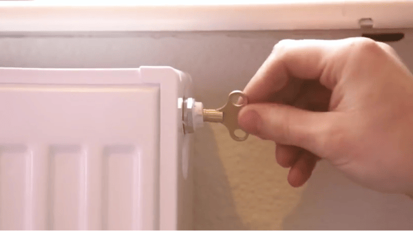 A man opening the air vent to a radiator with a radiator bleed key