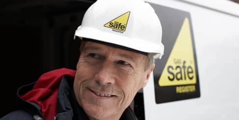A Gas Safe engineer leaving his van with a smile on his face and a hard hat on his head