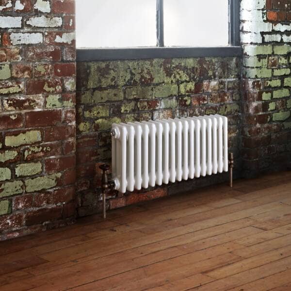 white column radiator under a window on a brick wall