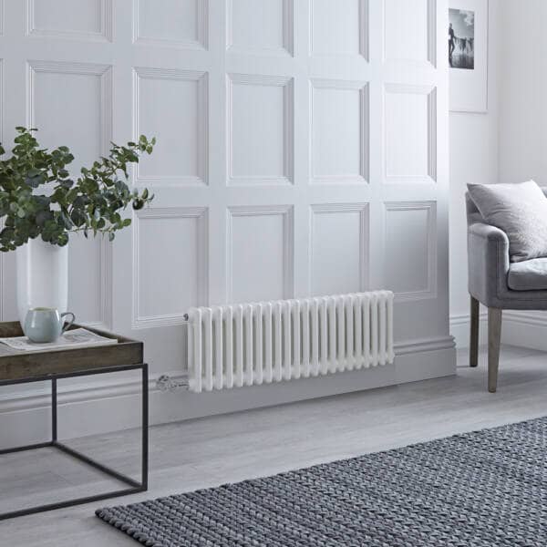 A white Milano Windsor horizontal electric radiator on a white wall next to a grey chair and wooden table. 