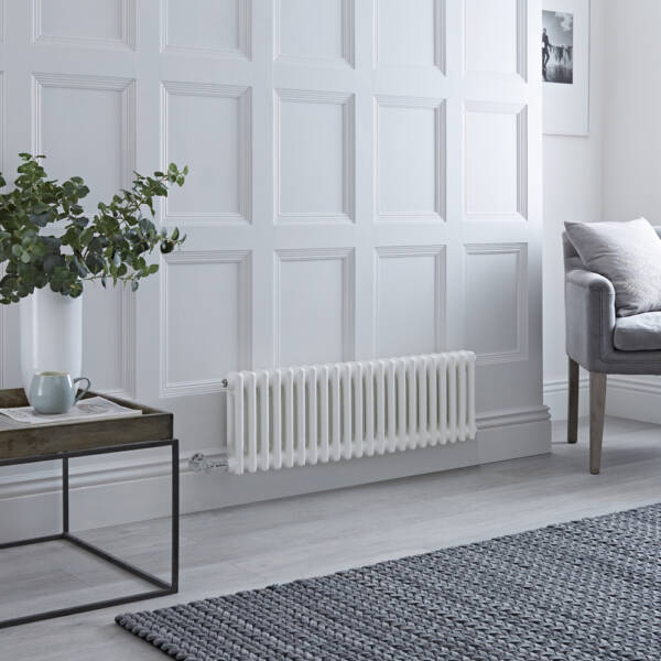 A white Milano Windsor horizontal electric radiator on a white wall next to a grey chair and wooden table. A white Milano Windsor horizontal electric radiator on a white wall next to a grey chair and wooden table.