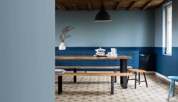 A dining room painted blue with a long dining table and benches