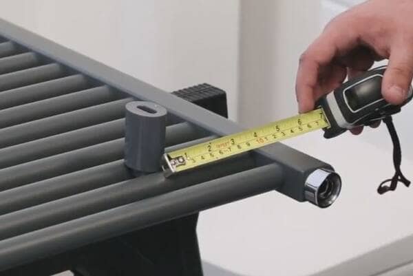 man measuring the distance between the centre of a bracket and the edge of a heated towel rail