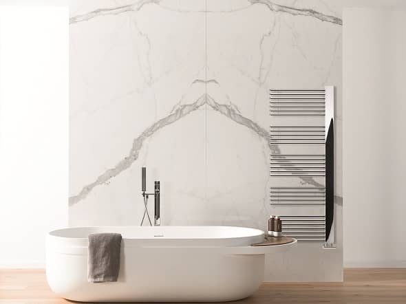 The Lazzarini Way Grado heated towel rail on a marble wall in a bathroom with a freestanding bathtub
