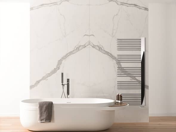 The Lazzarini Way Grado heated towel rail on a marble wall in a bathroom with a freestanding bathtub The Lazzarini Way Grado heated towel rail on a marble wall in a bathroom with a freestanding bathtub