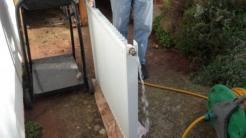 a radiator being flushed with a garden hose to clean out the inside of the radiator