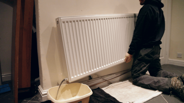 A man pouring away the contents of a radiator into a washing up bowl