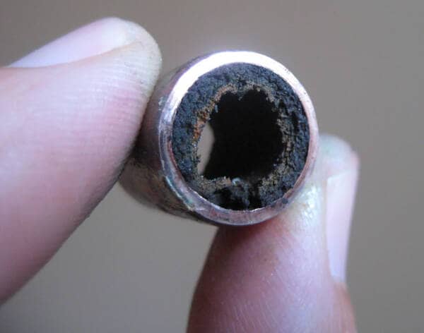 a picture of fingers holding a pipe that is filled with sludge and sediment