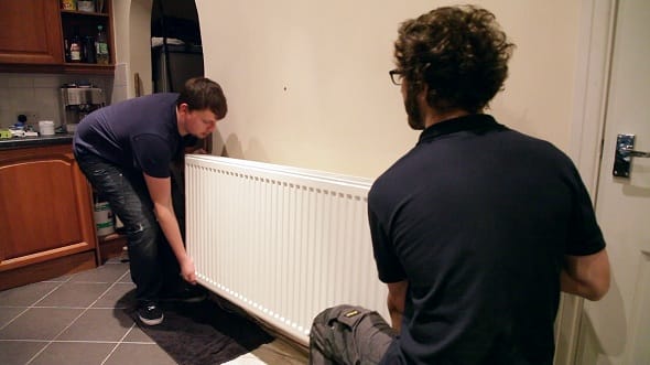 two men lifting a radiator from its mounting on a wall two men lifting a radiator from its mounting on a wall