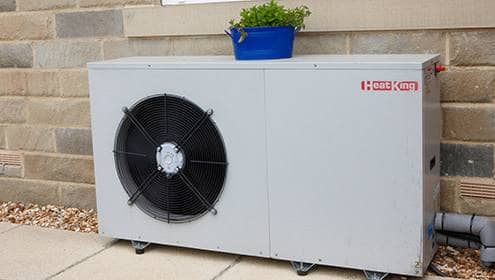 Large light grey air source heat pump with plant sat on top of it