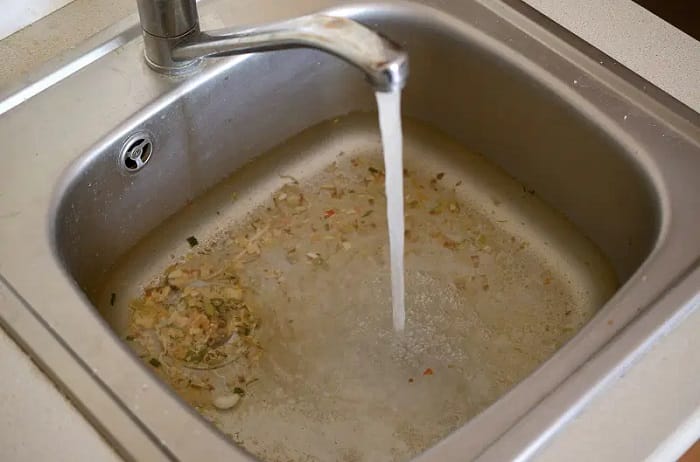Silver sink and running tap cleaning debris in sink Silver sink and running tap cleaning debris in sink