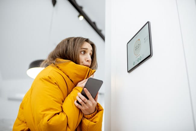 Woman in yellow coat looking at digital thermostat A woman wrapped up against the cold after her boiler stops working in winter