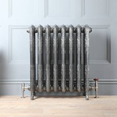 A metallic cast iron radiator against a grey panelled wall