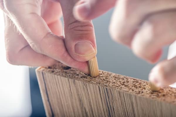 Man assembling furniture at home, hand with wooden dowel pins Man assembling furniture at home, hand with wooden dowel pins