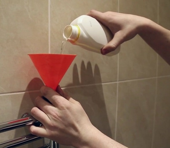 A man uses a funnel to carefully pour radiator inhibitor into a towel radiator