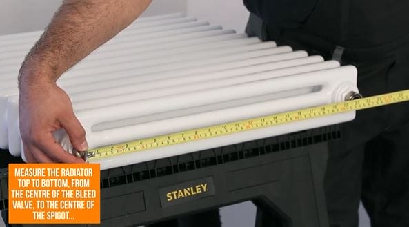 hand holding a tape measure against a radiator