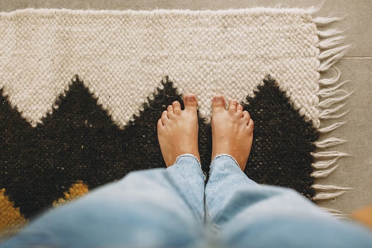 Feet on cosy woolen rug on background of concrete floor. Woman barefoot standing on modern rug in comfortable stylish home, top view. Cosy warm moments