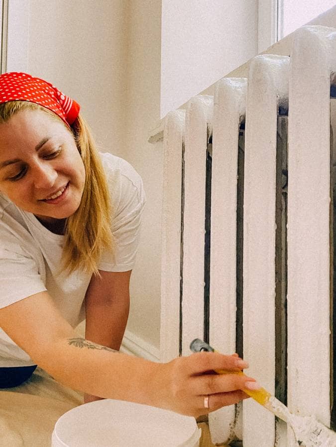 Woman painting radiator with white brush