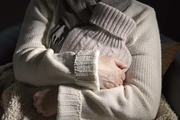 Mature woman holding hot water bottle to keep warm instead of using her heating system Mature woman holding hot water bottle to keep warm instead of using her heating system