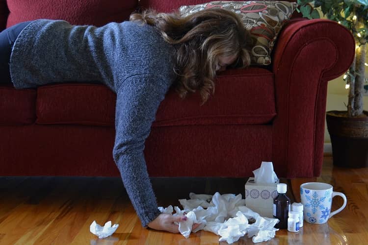 a woman with a cold laying face down on a sofa and surrounded by tissues