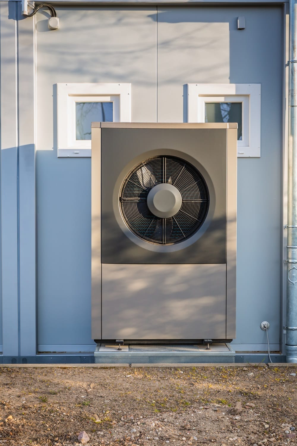 Grey air source heat pump fit outside a house with light walls and double small windows