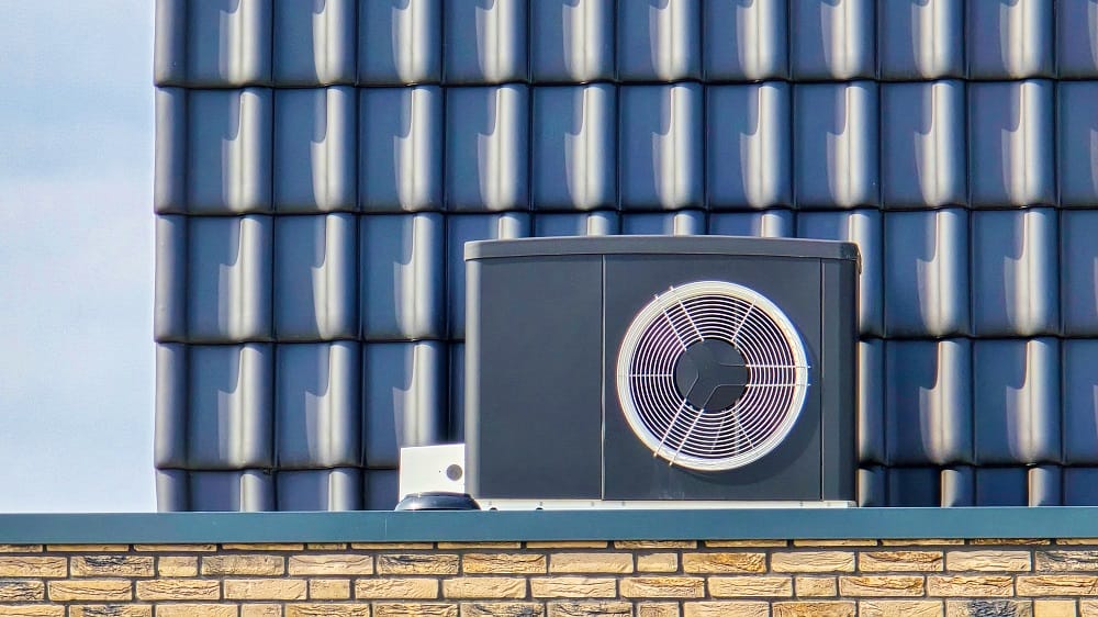 Black air source heat pump unit installed on rooftop of home with modern solar panels