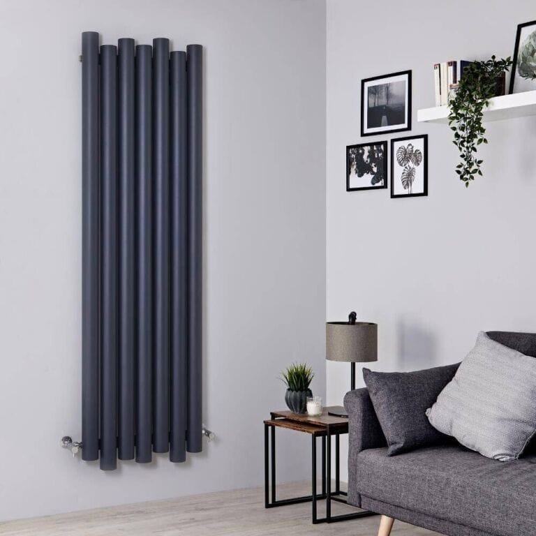 Milano Motus black aluminium vertical designer radiator on white wall nearby multiple framed art pictures and shelf with houseplant above grey settee and small table with lamp