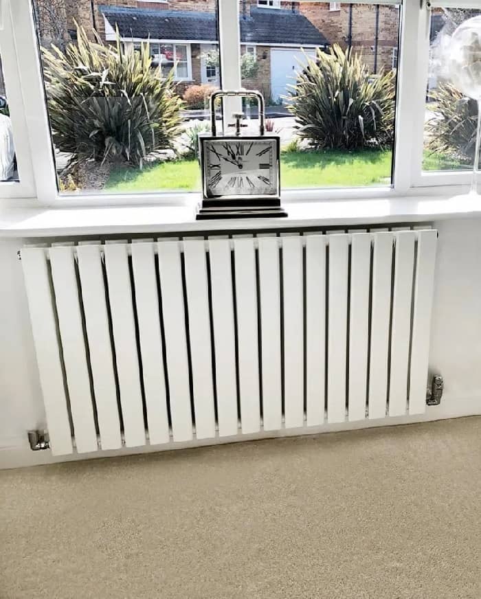 A white Milano Alpha designer radiator on a white wall under a window.
