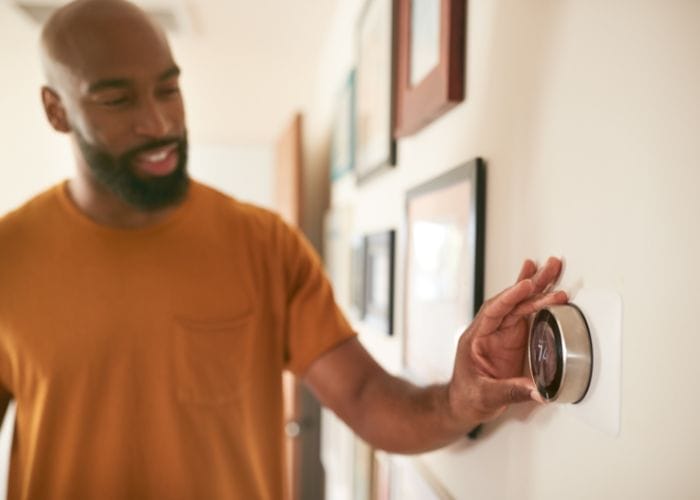 man adjusting modern thermostat on wall of home