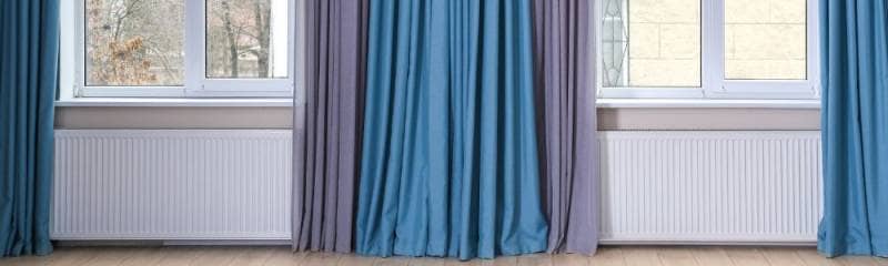 two radiators under windows with blue curtains hanging over