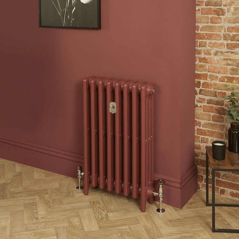 Milano Mercury eating room red four column cast iron radiator on red wall background and wooden floor nearby small table with candle and houseplant