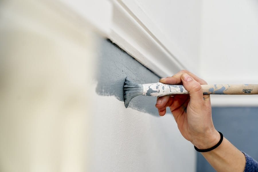Close up image of hand painting wall with thin paintbrush