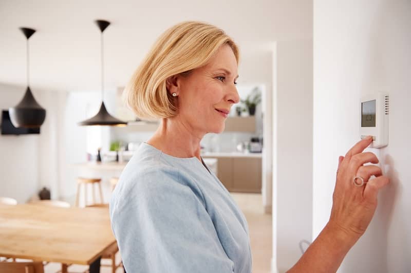 a lady adjusting the temperature of the heating from her sitting room thermostat