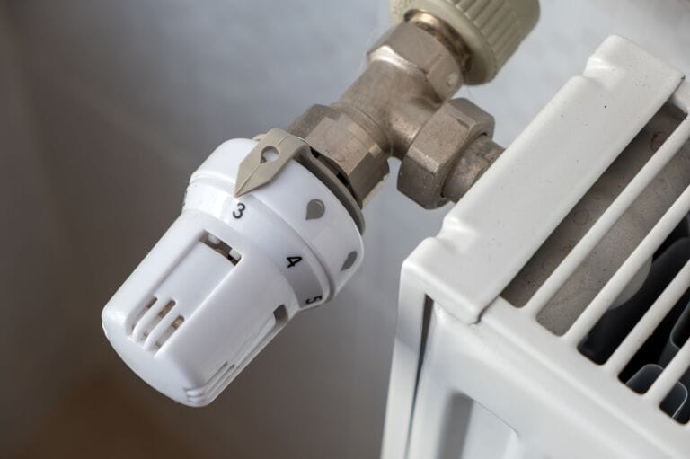 Close-up image of white radiator valve with gold attachment on white convector radiator