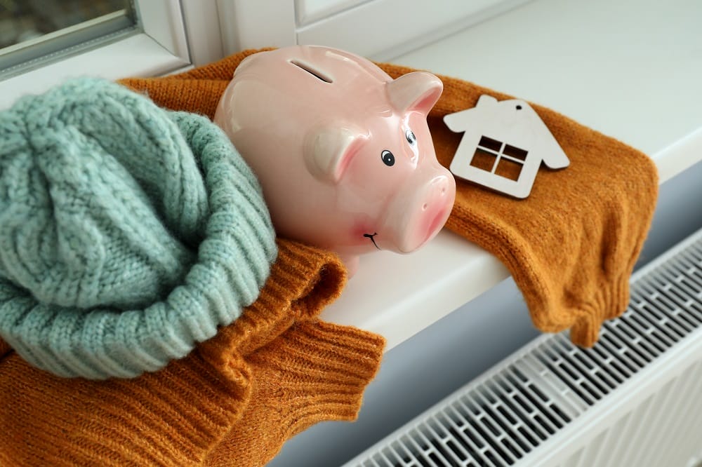 Piggy bank and warm jumper and wolly hat with home motif on a ledge above white convector radiator