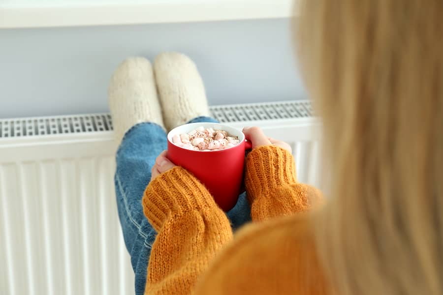 Woman sat with a hot chocolate warming feet on a radiator