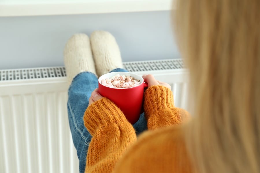 Woman sat with a hot chocolate warming feet on a radiator Woman sat with a hot chocolate warming feet on a radiator