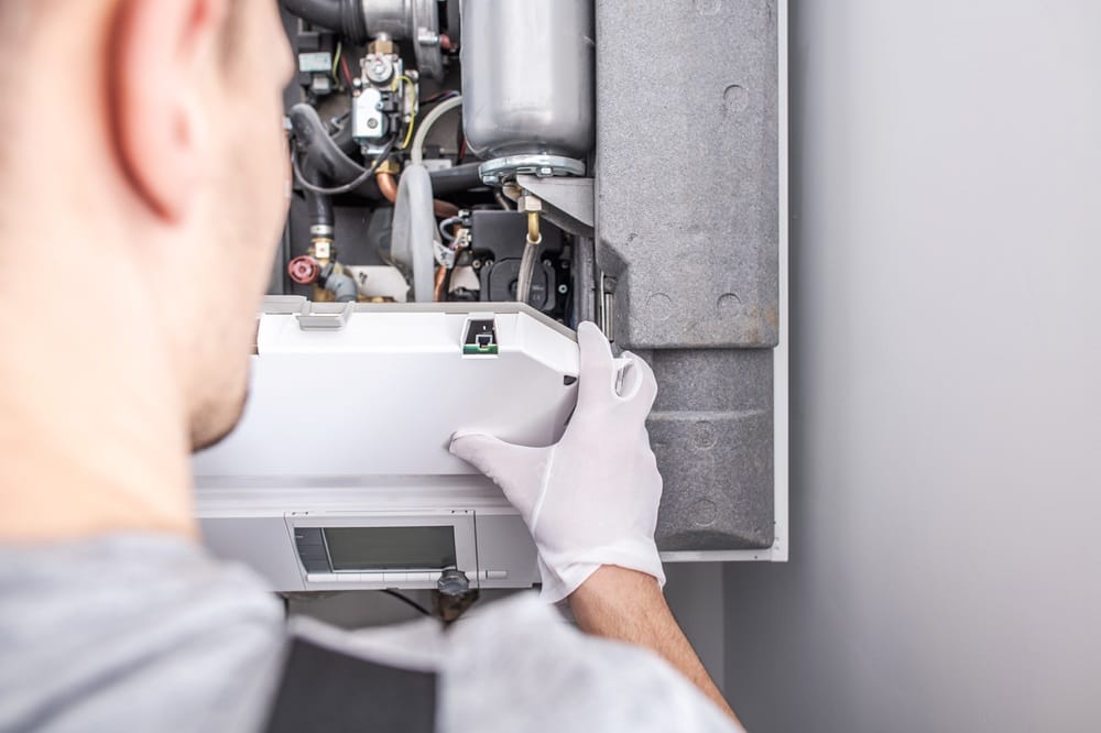 Contractor wearing white safety gloves repairing a central heating system attached to a wall