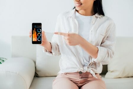 Latin woman holding smart phone with various heating charts on digital display