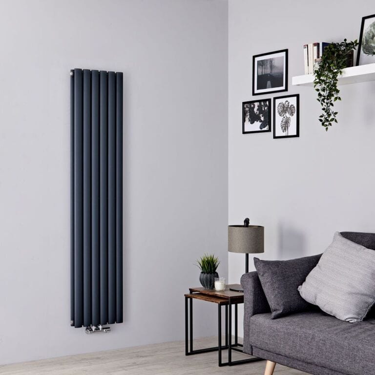 Milano Aruba Flow anthracite vertical double panel middle connection designer radiator on white wall nearby grey settee beneath shelving and multiple framed art pictures