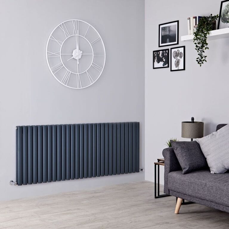 Milano Aruba anthracite horizontal designer double radiator on white wall beneath large clock adjacent to grey settee beneath shelving and artwork