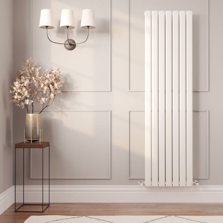 Milano Alpha white vertical flat single panel designer radiator on light wall above white skirting board nearby small table with vase with fake plant beneath triple light fitting