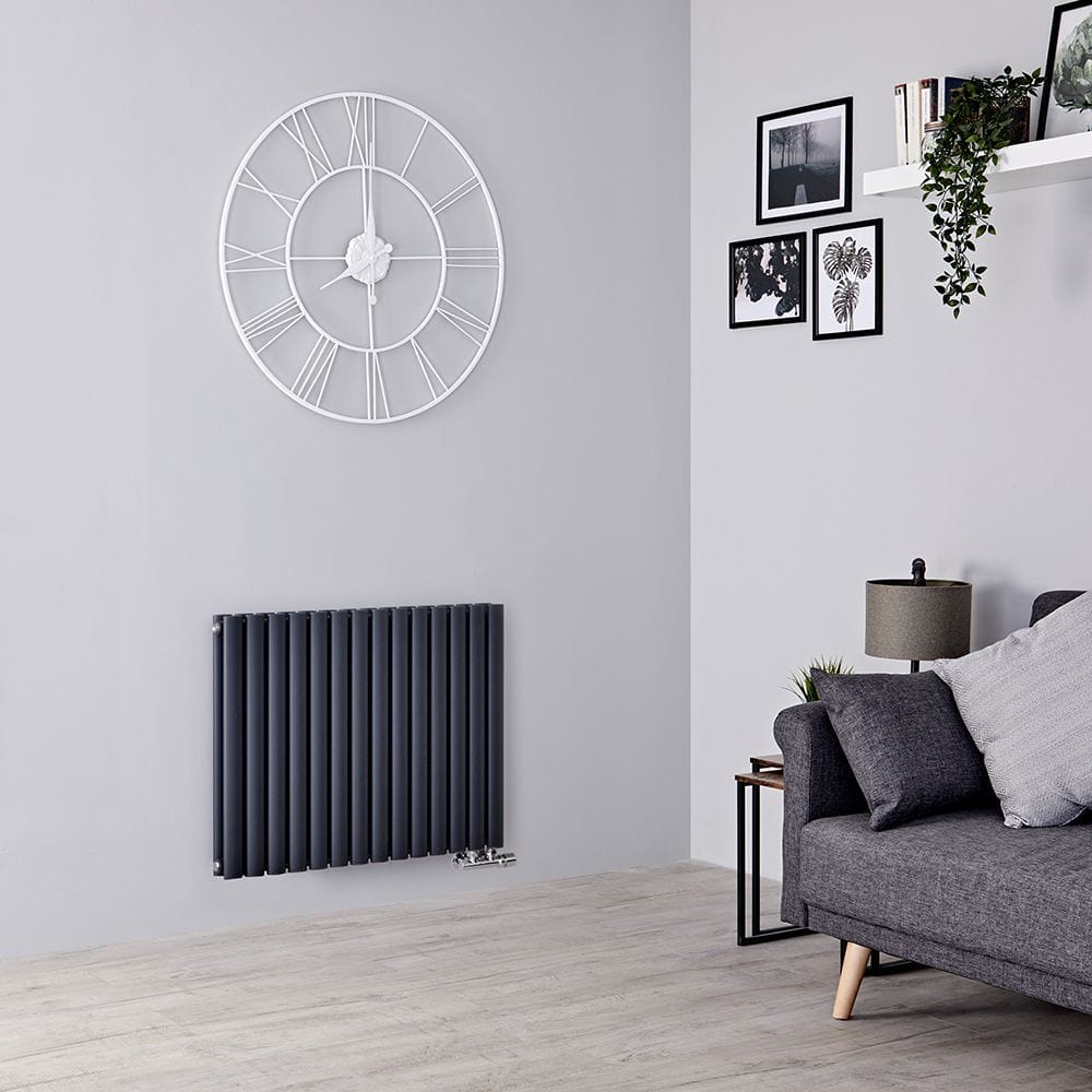 Milano Aruba Flow anthracite horizontal side connection designer radiator on white wall beneath clock adjacent to wall with artwork and shelving and grey settee